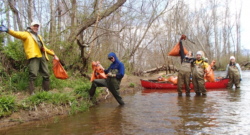 People standing in or near ankle-deep water hold full trash bags as part of service project. 